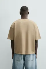 Sudadera de manga corta color beige, con cuello redondo y corte relajado. Presenta un bordado y estampado en el pecho con texto y un diseño floral.