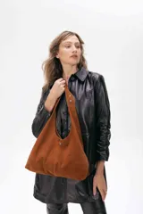 Cartera tipo hobo de cuero ovino color suela, con diseño amplio y flexible. Presenta un aplique metálico pequeño en el frente y costura central vertical.