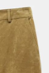 Pantalón de piel color tostado, tiro medio con cierre frontal de cremallera y botón, bolsillos delanteros y traseros, y bajo con acabado de pliegues.