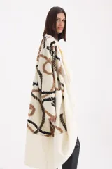 Spolverino largo de tejido de punto en color crudo, con diseño de patrones geométricos en tonos marrón y negro. Presenta un corte abierto con solapas amplias y mangas largas.
