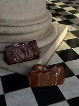 Cartera tipo tote de cuero color chocolate, con tachas plateadas en los bordes y bolsillo externo con cierre imantado. Incluye sobre interno grande con gancho.