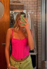 Corset o top estilo bustier color fucsia, con tirantes finos y detalles de encaje o tejido calado. Presenta un escote festoneado y un corte ajustado que termina en pico en la parte inferior.