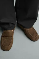 Mocasines de piel con acabado serraje y suela ultrafina, color marrón. Presentan detalle de bordón y antifaz en el empeine con costuras pespunteadas, forro interior de piel y horma cuadrada.