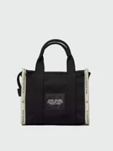 Bolso tipo tote Marc Jacobs modelo The Small Tote, color beige con detalles y texto en negro que dice "THE TOTE BAG MARC JACOBS". Cuenta con asas superiores y laterales para llevar en la mano o al hombro.