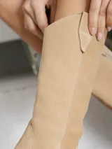 Bota texana de caña media color beige, confeccionada en gamuza con detalles de costuras decorativas en el empeine y caña. Tiene cierre lateral y taco de madera.