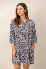 Vestido corto camisero color beige con estampado floral azul marino, cuello camisero, cierre frontal con botones, mangas tres cuartos y bolsillos laterales.