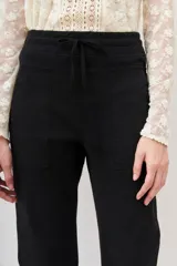 Pantalón tipo babucha de gabardina elastizada, color negro, con cintura elástica ajustable mediante cordón, puños en los tobillos, bolsillos diagonales frontales y bolsillos traseros con solapa y botón.