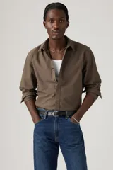 Camisa de manga larga color marrón oscuro, con cuello clásico y cierre frontal de botones. Se lleva abierta sobre una remera blanca de algodón acanalado.