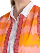 Chaleco sin mangas estilo boho, con estampado de ondas en tonos naranja, rosado y amarillo. Presenta bordes con detalles geométricos en color bordó y cierre frontal abierto.