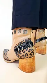 Bota tejana de cuero, combinada en color tostado, animal print de leopardo y puntera en charol negro. Cuenta con taco de madera, detalle de hebilla lateral y ojales metálicos en la parte superior.