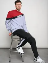 Buzo de hombre con diseño de bloques de color, combinando rojo en la parte superior de los hombros y gris melange en el cuerpo. Presenta una franja diagonal negra con el logo Umbro en blanco cruzando el pecho.