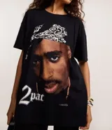 Remera negra de algodón con cuello redondo y manga corta, presentando un estampado grande y detallado del rapero Tupac Shakur con un pañuelo blanco en la cabeza.
