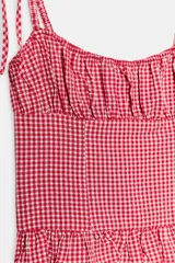 Top de escote redondo y tirantes finos con lazada, con estampado de cuadros vichy en rojo y blanco. Presenta frunces en el pecho y detalle de volados en el ruedo.
