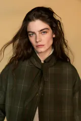 Chaqueta de algodón encerado con diseño de cuadros en tonos verde oliva, beige y líneas rojas. Presenta cuello solapa, cierre frontal con botones a presión metálicos, bolsillos de plastrón con solapa y un detalle de pañuelo desmontable sobre los hombros.