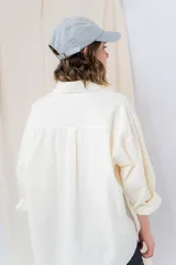 Camisa verde pastel de algodón, corte oversize, con cuello camisero, cierre con botones, mangas largas con puños con volados de encaje blanco, dos bolsillos frontales con solapa y ruedo irregular. 