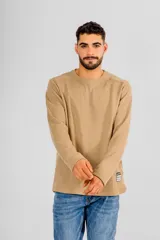 Buzo de manga larga con cuello redondo, confeccionado en tejido de punto con textura tipo waffle. Presenta un diseño minimalista con una pequeña etiqueta decorativa en el ruedo inferior.