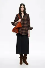 Camisa de corte recto y largo medio, confeccionada en tejido de algodón con textura. Presenta un diseño de cuadros en tonos rojo, negro y azul, cuello camisero, cierre frontal con botones, manga larga con puños abotonados y bolsillo de plastrón en el pecho.