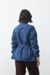 Sobrecamisa de jean color negro con silueta relajada, cuello camisero, cierre frontal con botones metálicos, bolsillos frontales y cinturón ajustable en la cintura.