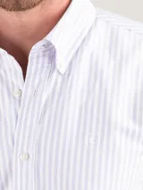 Camisa de hombre oxford con diseño de rayas verticales celestes y blancas, corte regular fit, cuello button-down, manga larga y cierre frontal con botones.