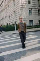 Jersey de punto con cuello polo y cierre frontal de botones. Presenta un diseño de estampado de rombos en el frente en tonos gris y blanco sobre una base color marrón.