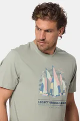 Remera de manga corta color verde grisáceo con cuello redondo. Presenta un estampado frontal de veleros sobre un fondo circular con líneas verticales, y texto bordado debajo.