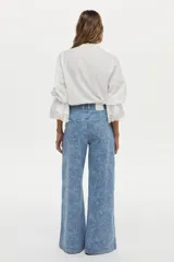 Camisa blanca de algodón con cuello alto, detalles de encaje broderie en el frente, mangas abullonadas y puños con volados y encaje. Cierre frontal con botones tapados.
