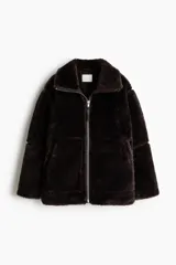 Abrigo de corte oversized confeccionado en tejido de efecto piel sintética suave. Presenta cuello elevado, cierre frontal con cremallera, hombros caídos, costuras visibles en los codos y bolsillos laterales al bies. Incluye forro interior.