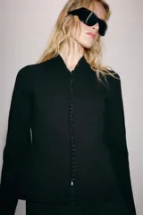Chaqueta de punto negro con escote en V y manga larga. Cierre frontal con una hilera de pequeños botones forrados.