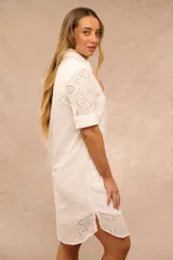 Vestido midi blanco de broderie, de corte recto con cierre frontal de botones, cuello camisero y mangas cortas.