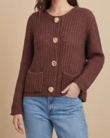 Saco de punto tejido con textura acanalada, color marrón chocolate. Presenta cuello redondo, cierre frontal con botones grandes de diseño circular, mangas largas y dos bolsillos frontales aplicados.