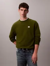 Buzo de cuello redondo Calvin Klein confeccionado en algodón regenerado de color verde militar, con interior de tejido terry, puños y cuello con punto canalé, y un pequeño parche con el monograma de la marca en el pecho.