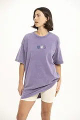 Remera de corte oversize y estilo vintage con efecto lavado, color violeta, con cuello redondo y estampa pequeña central con motivos florales y geométricos.