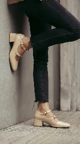 Zapatos tipo Mary Jane color off-white, confeccionados en cuero con acabado brillante. Presentan doble tira con hebillas metálicas sobre el empeine, punta redondeada y taco cuadrado bajo.