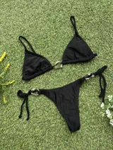 Conjunto de bikini negro con corpiño triangular con argolla metálica y bombacha colaless con tiras para atar y argollas en los costados.