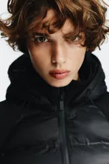 Chaqueta acolchada negra con cuello subido y capucha ajustable con cordones elásticos y stopper. Mangas largas combinadas en tejido efecto neopreno. Bolsillos laterales y cierre frontal con cremallera termosellada.