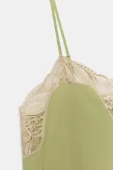 Vestido midi de satén color verde oliva, con escote recto y tirantes finos ajustables. Presenta detalles de encaje en color crema en el escote y en el bajo, con aberturas laterales.
