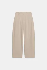 Pantalón de tiro bajo color beige, de pernera holgada tipo barrel que se estrecha hacia el tobillo, con bolsillos delanteros y presillas para cinturón.
