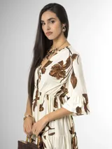 Vestido largo color crudo con estampado floral marrón, escote en V cruzado, mangas tres cuartos con volados y falda con niveles fruncidos.