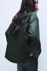 Camisa oversize de popelín de algodón, color verde oscuro, con cuello solapa, manga larga con puños abotonados y cierre frontal con botones.