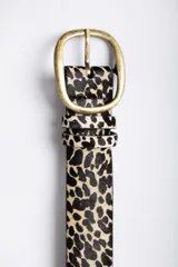 Cinturón de cuero con textura de pelo y estampado animal print de leopardo. Cuenta con una hebilla metálica de tono bronce envejecido y dos pasadores a juego.