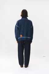 Campera de tejido de punto color marrón con destellos de lurex, corte oversize y cierre frontal. Presenta detalles de costuras y terminaciones en color crema, cuello alto y bolsillos frontales.