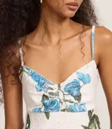 Vestido corto de corte evasé confeccionado en tejido laise con estampa tropical de flores azules y hojas verdes. Presenta escote en V, breteles finos ajustables y diseño con perforaciones caladas características del broderie.