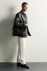 Bolso de mano y hombro color negro, con diseño estructurado, solapa frontal y cierre metálico. Cuenta con asa superior de mano y un compartimento principal amplio.