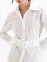 Camisa Oslo de poplín de algodón color blanco, con silueta estructurada, cuello camisero amplio, manga larga y cinturón ancho incorporado con hebilla rectangular forrada.
