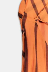 Vestido midi de color naranja con rayas diagonales marrones, escote fluido y tirantes finos cruzados en la espalda con abalorios. Presenta corte evasé con abertura frontal y forro interior.