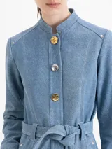 Tapado de cuero ovino color azul, con acabado símil denim. Tiene largo 7/8, cuello mao y cierre frontal con broches metálicos dorados y plateados. Incluye un lazo decorativo del mismo cuero en la cintura, mangas largas y vuelo hacia el ruedo. Cuenta con bolsillos ojal en los laterales.