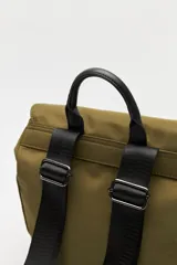 Mochila urbana de nylon color beige, con solapa superior, bolsillo frontal con cierre y correas decorativas con hebillas metálicas. Incluye manija superior y correas ajustables.