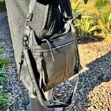 Bolso tipo morral y bandolera de eco-cuero negro, con cierre superior, bolsillos frontales con cierre y correa ajustable para el hombro.