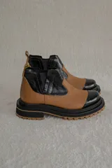Botas tipo Chelsea de caña corta con diseño bicolor en tonos marrón y negro. Presentan paneles elásticos laterales, puntera reforzada y suela track robusta con plataforma.