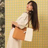 Cartera tipo tote de cuero sintético con diseño combinado en tono gris y blanco, textura granulada, asas largas para el hombro y cierre superior.